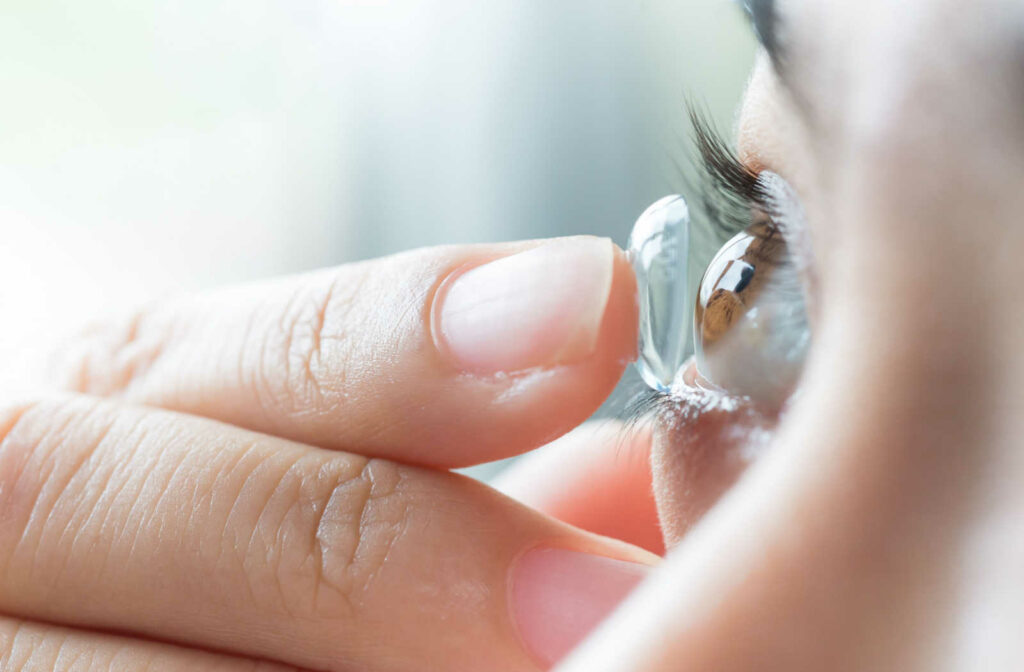 A close up photo of a woman putting a contact into her right eye.