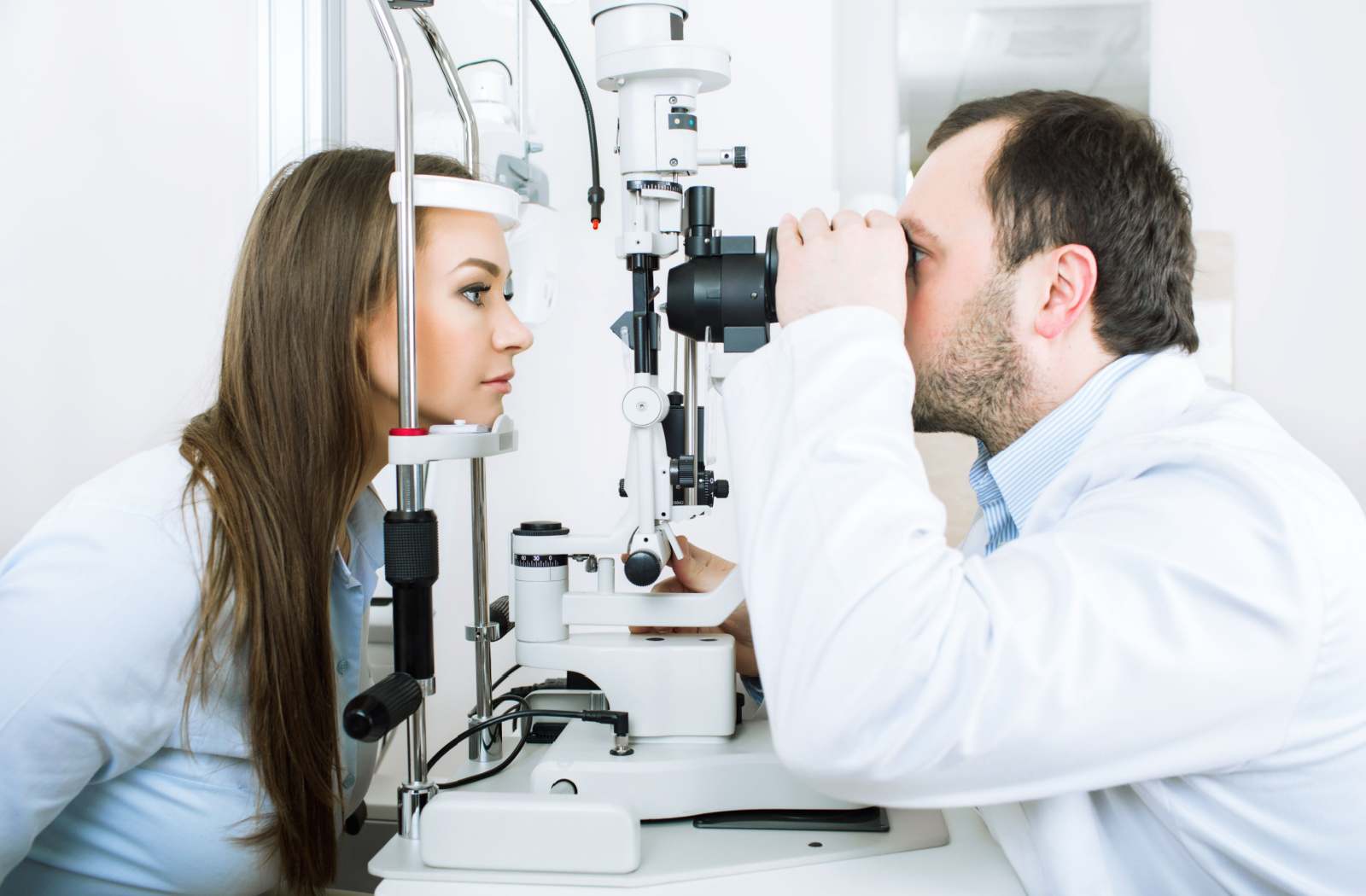 Male optometrist examines female patient with a slit lamp.