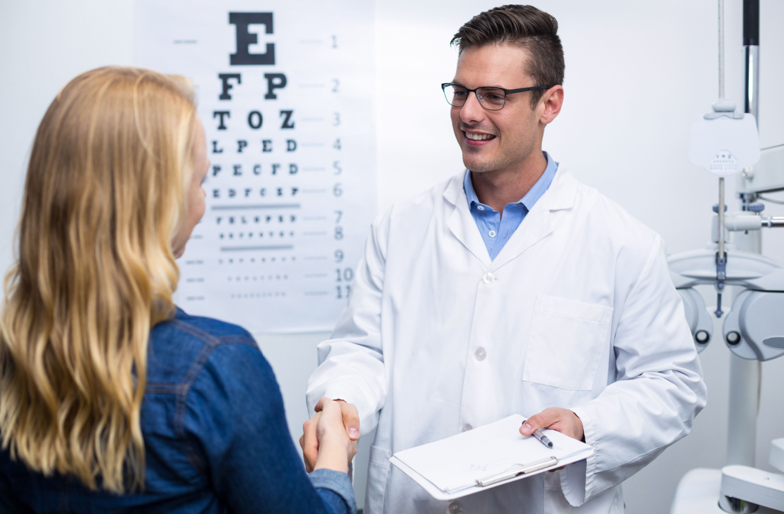 A woman in an optometry clinic shaking hands with her male optometrist.