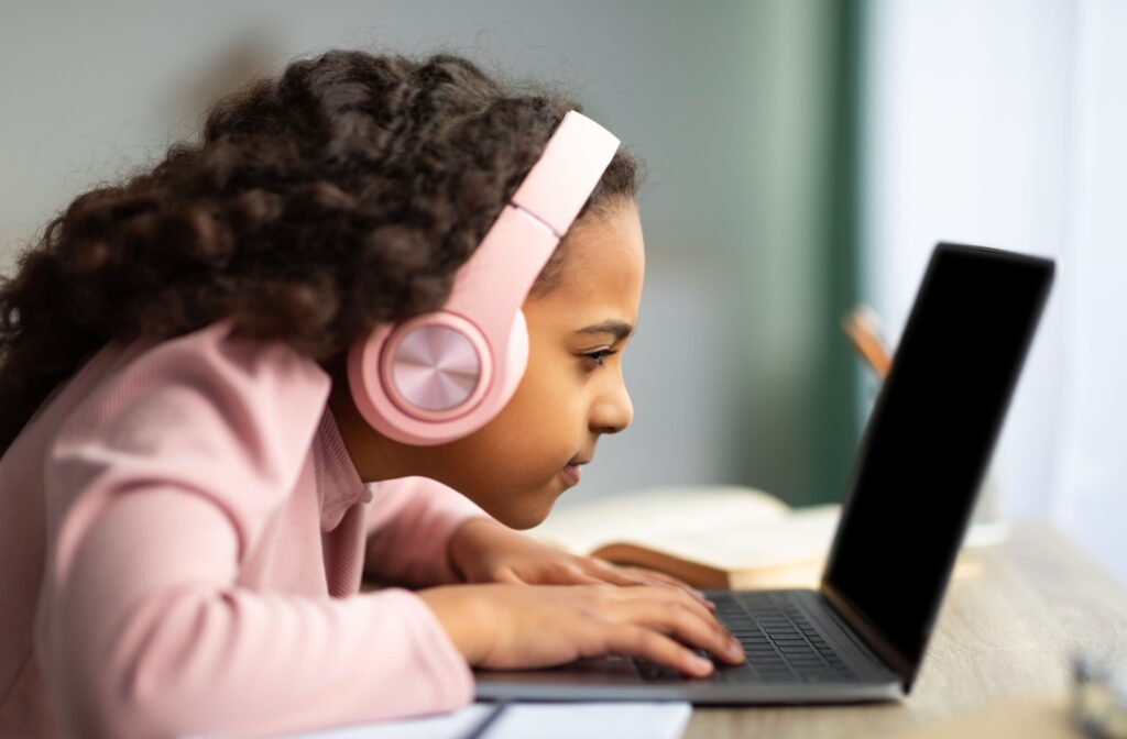 A young girl with headphones sitting and leaning closer to a laptop to see.