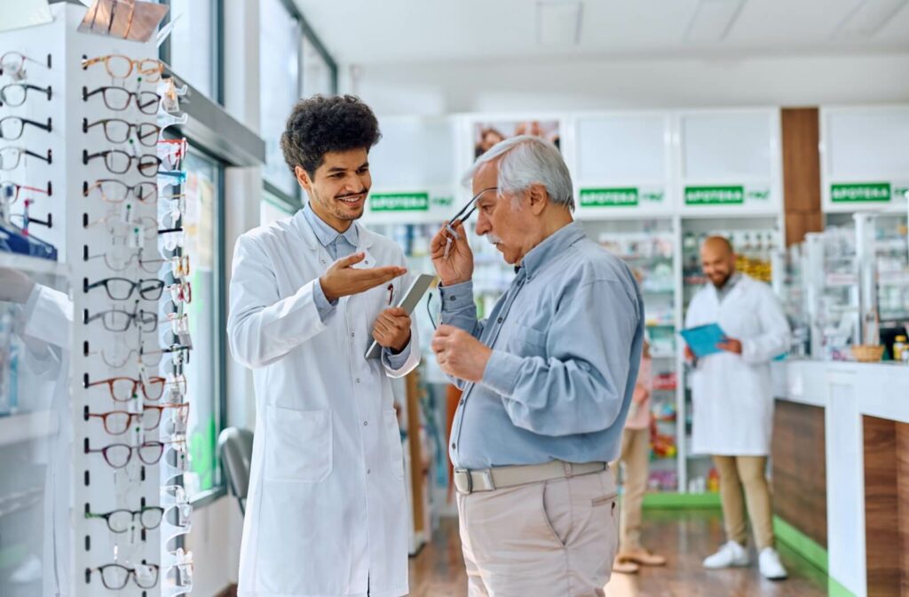 A senior tries on a new pair of glasses with the help of an optometrist in a bright and well-lit pharmacy