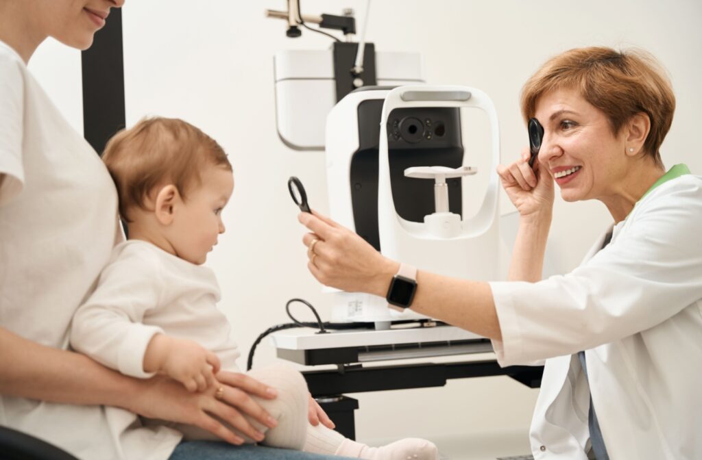 An infant sitting on their parent's lap while a smiling optometrist checks their vision during an eye exam.