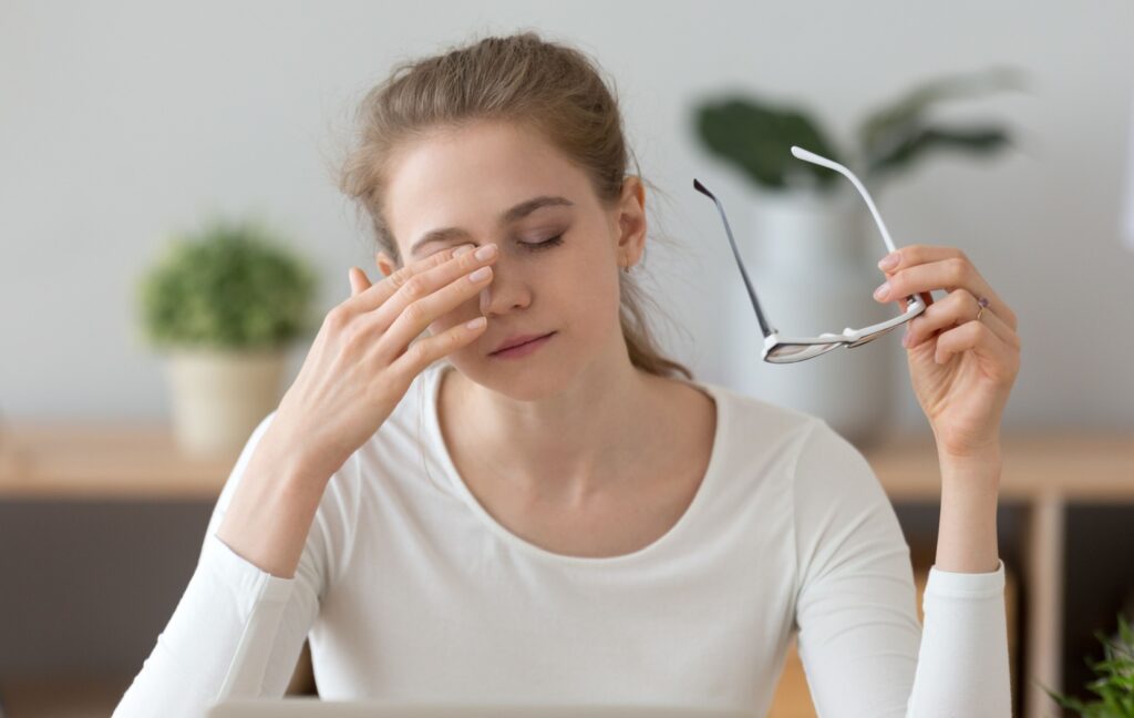 A young person with weak eye muscles removes their glasses and rubs their tired, sore eyes.