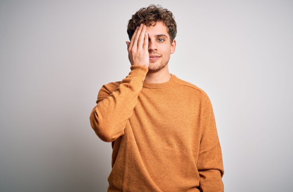 A person on a white background covers one eye with their hand.